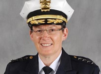 White woman in wire-rimmed glasses smiling in a pose with a police hat and uniform on