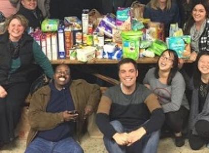 Lots of people smiling and sitting around a table posing for the camera, board games on the table