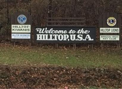 Long outdoor sign in front of trees saying Welcome to the Hilltop USA
