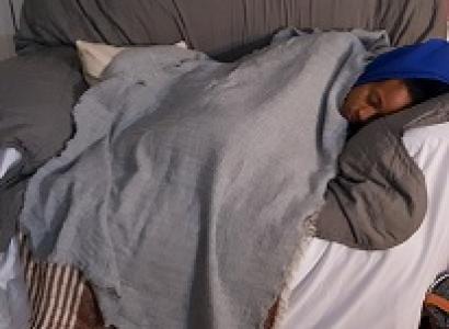 Young black woman asleep under huge blanket on a gray loveseat