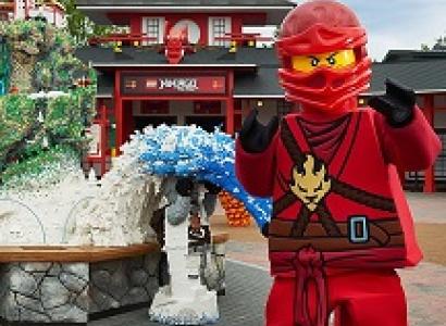 Robot looking character in red suit and helmet standing by and in front of structures made out of legos