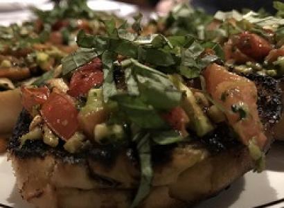 A piece of food on a plate with other similar items, looks like a baked potato with lots of greens, tomatoes, other brownish things on top.