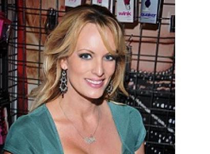 White woman with long blonde hair and large breasts with lots of cleavage in a green dress smiling