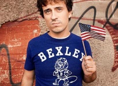 Young white man with brown hair and a Bexley T-shirt holding a small American flag
