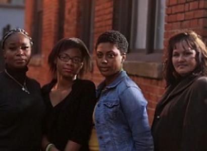 Three black women and a white woman standing outside looking very serious