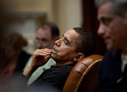 Obama leaning back in leather chair with hand on mouth looking pensive
