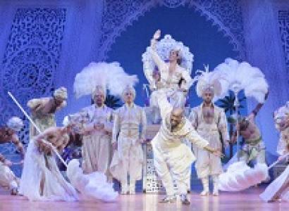 Fancy costumed people against blue theater backdrop like a castle inside, feathered headdresses, dancing