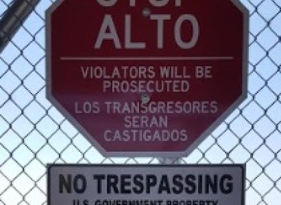 Stop sign in Spanish on a wire fence and sign that says No Trespassing