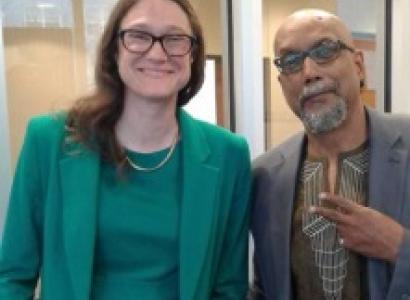 Tall thin white woman smiling with glasses and a green dress next to an older black man in a suit making a peace sign