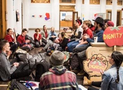 Dozens of kids sitting around an office with a tomato sign that says Dignity