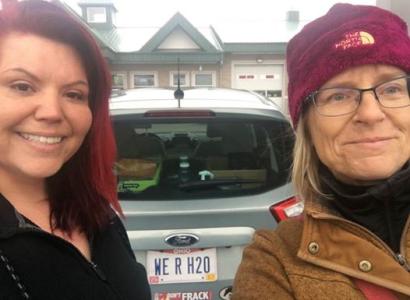 Carolyn on the right, blonde woman with maroon winter hat and glasses standing next to car with Native American woman on right