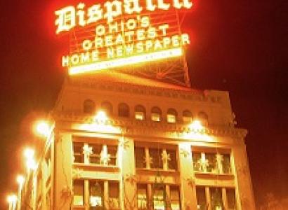 Bright yellow and red neon sign saying Dispatch Ohio's greatest homes newspaper above a big fancy building at night