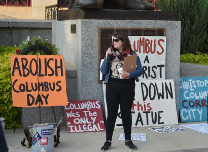 Woman in front of signs talking into a microphone