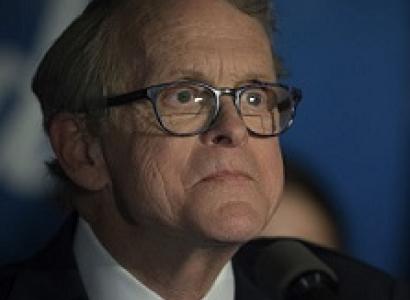 Older white man with glasses looking weird and crazy in a suit at a microphone