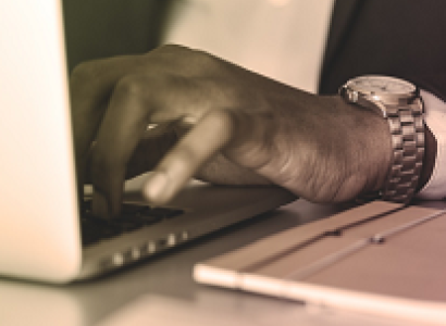 Extreme close up of black man's hand wearing a watch typing on a laptop