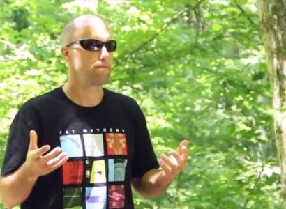 Young white man mostly bald holding his hands out in front of him standing in a forest