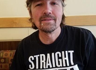 Man with brown hair sticking out from a red baseball cap and goatee wearing a black T-shirt 