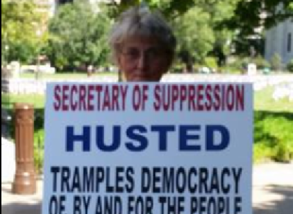 Woman holding sign against Jon Husted
