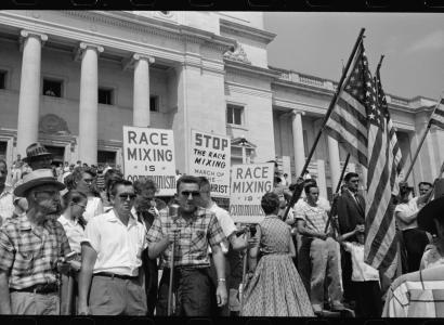 Black and white photo of protest in streets from 50s with sign saying something about race mixing
