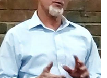 Bald white man with glasses with white goatee talking and making hand gestures