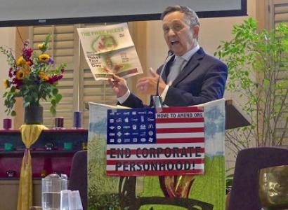 Dennis Kucinich, 60-ish white guy in a suit at a podium holding up a copy of the Free Press