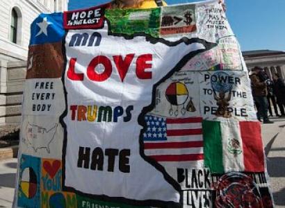 A woman protests Donald Trump with a "Love Trumps Hate" banner/blanket