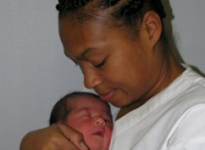Black woman with hair up in braids side view smiling with eyes looking down as she holds a newborn baby