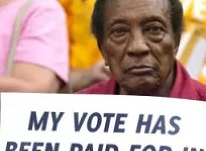 Black man holding a sign reading My vote has been paid for in BLOOD