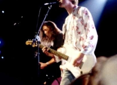 Kurt Cobain singing into a mic and a guitarist behind him