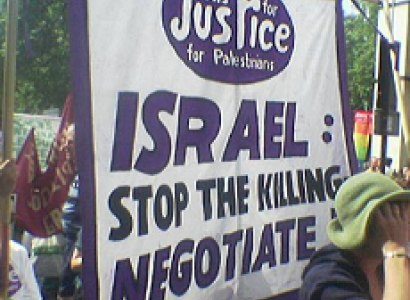 People protesting outside with sign saying Israel stop the killing, negotiate