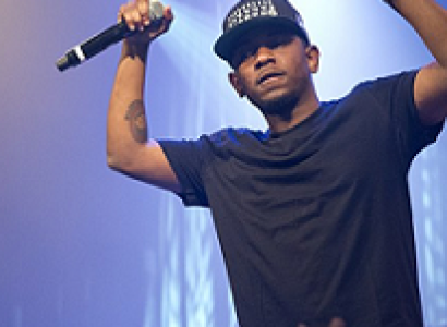 Black male rapper on stage with arms in air holding a mic
