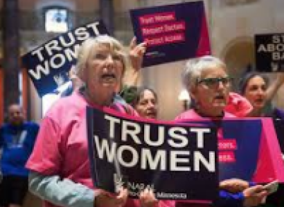 Two older women at a rally holding a sign saying Trust Women