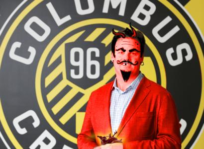 A Circle with the words Columbus Crew in it and the number 96 with cartoonish man wearing a red suite jacket in front with black hair and devil horns, mustache and goatee