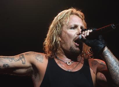 Vice Neil singing into mic with long stringy blonde hair and lots of tattoos