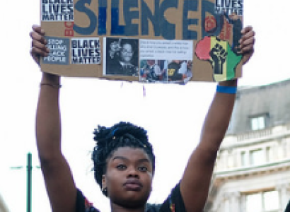 Black woman holding up a sign that says we will not be silenced