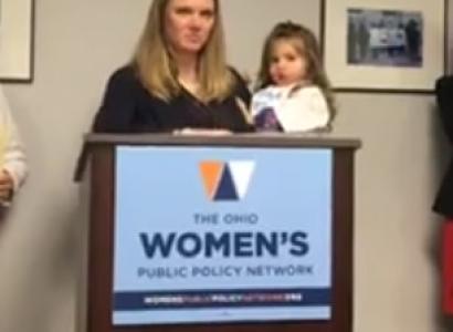 Woman holding a baby at a podium that says Women's Public Policy Network