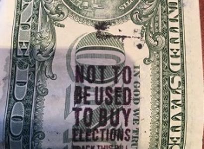 A close up of the back of a dollar bill with a stamp on it saying Not to be used to buy elections