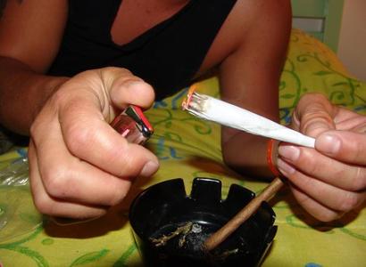 Person's hands lighting a huge joint over an ashtray