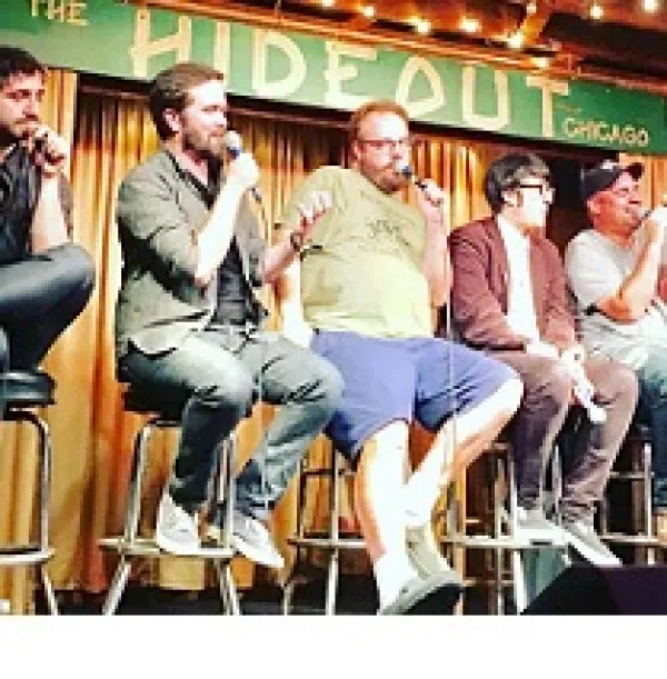 Different sizes and types of white guys sitting on stools on a stage, a couple talking into mics