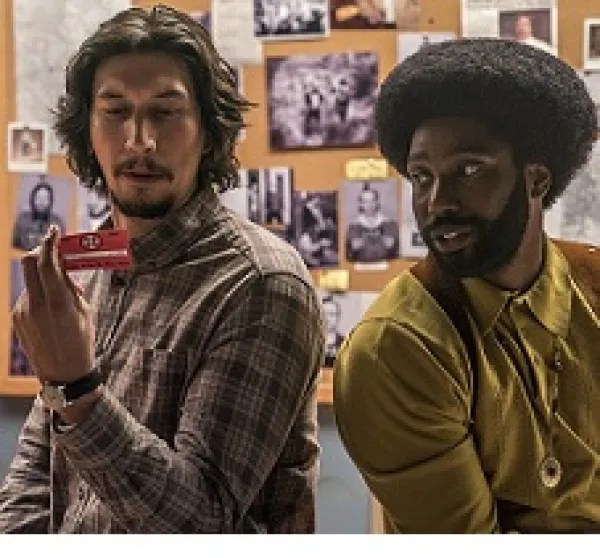 Young white man with dark hair and goatee sitting next to young black man with big afro and beard