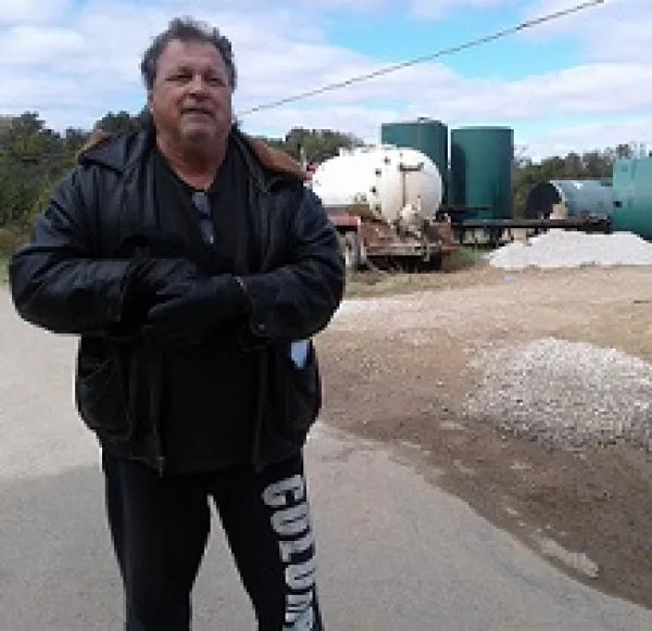 White man in winter coat standing in front of metal tanks and a truck