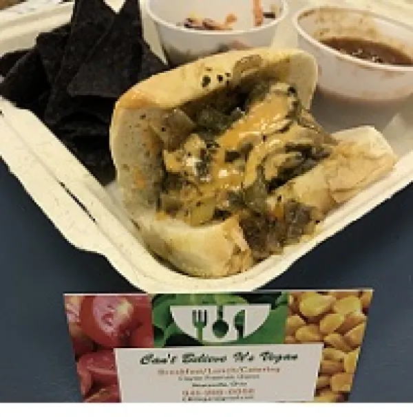 Sandwich in a carton with two bowls of food and a card in front that says Can't Believe It's Vegan