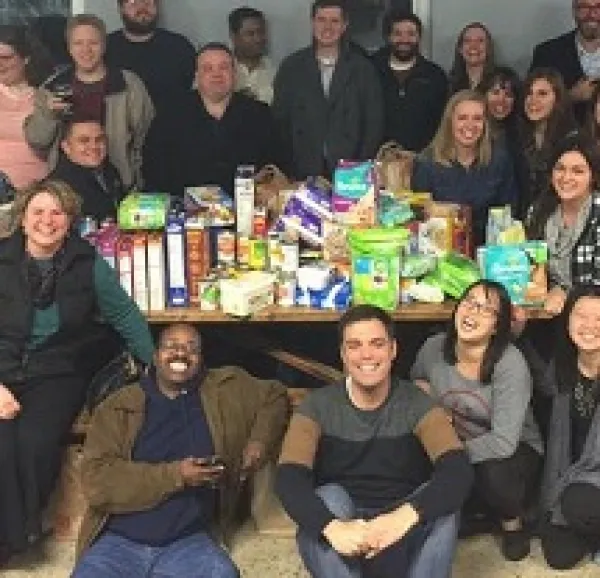 Lots of people smiling and sitting around a table posing for the camera, board games on the table