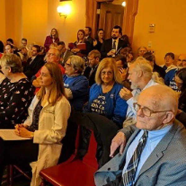 Lots of white people sitting in rows on wooden seats