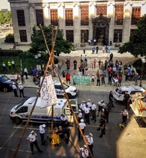 Crowd of protestors outside a big government building with a tripod looking wooden structure in the street