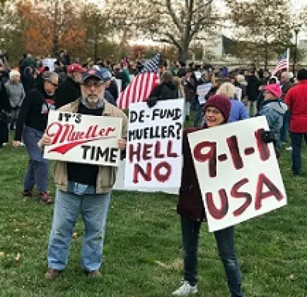 People outside gathered in a group holding signs that say It's Mueller Time, 9-1-1 USA