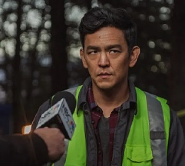 Man with dark hair and a yellow vest with a news media microphone aimed at him and he has a worried look on his face