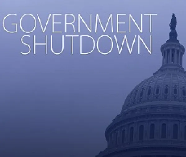 Blue background white letters saying Government Shutdown and the edge of the capitol building in DC