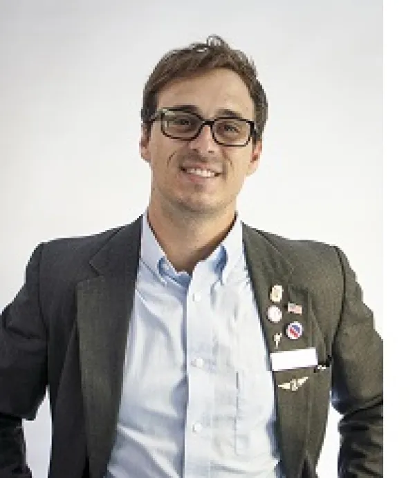 Young white man with dark rimmed glasses and a suit with lots of political buttons and a big smile