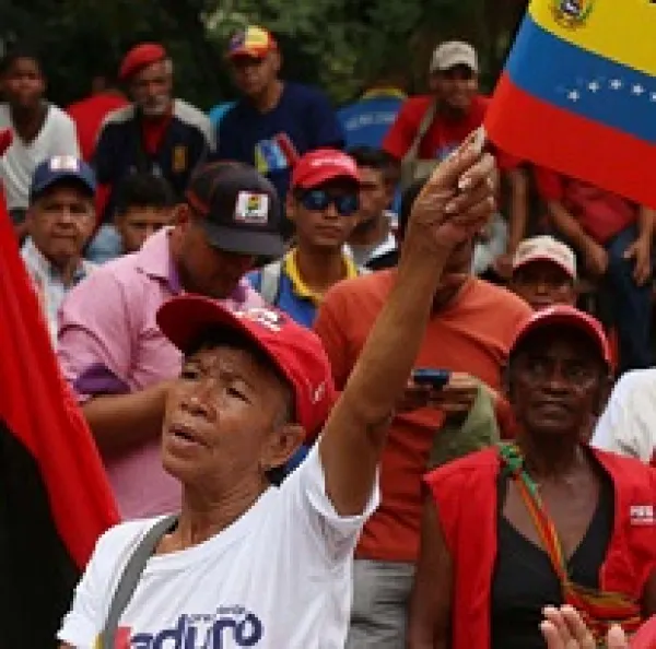 People of color outside at a rally one woman in front waving a red, blue and yellow striped flag